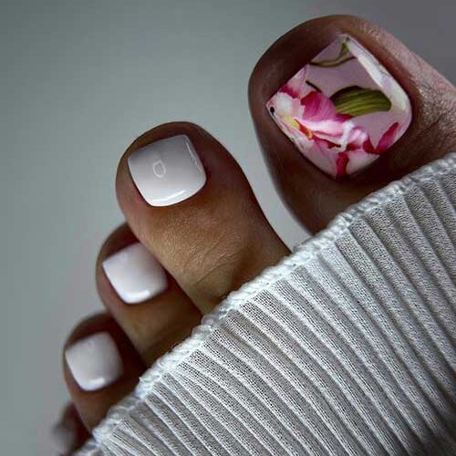 Glossy white toenails with a subtle pink big toenail decorated with pink flowers and green leaves