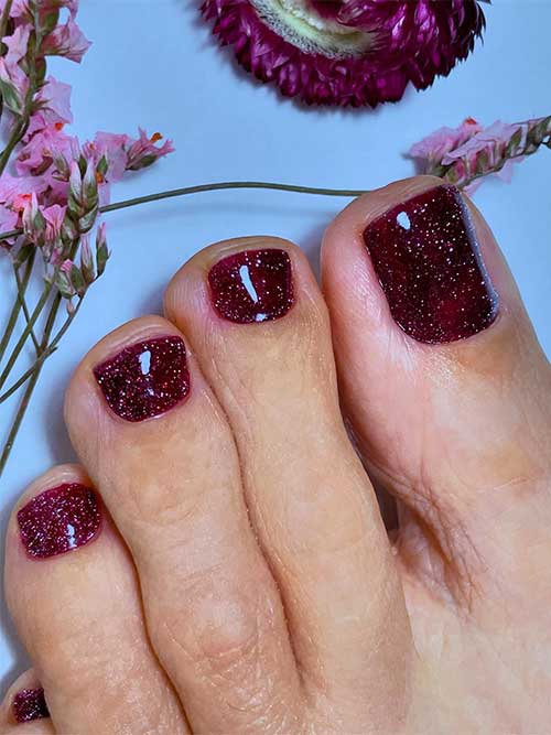 Elegant burgundy toenails adorned with glitter, showcasing a chic fall pedicure.