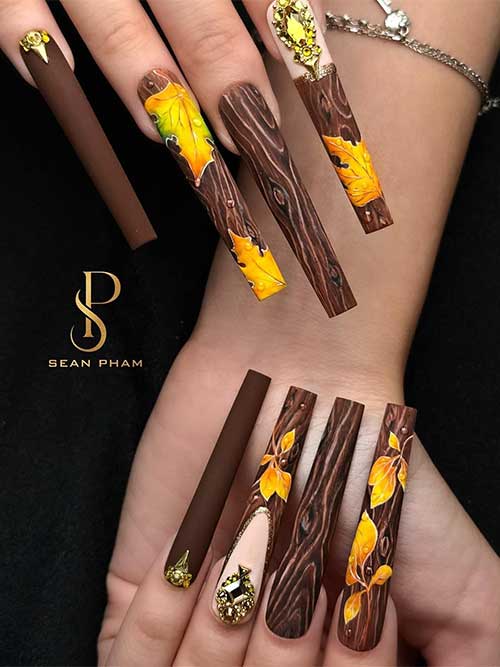 Extra long square brown nails featuring wood art and burnt yellow-orange maple leaves, accented with gold rhinestones.