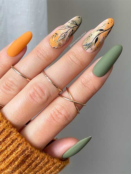 Matte green and burnt orange almond-shaped nails with black leaf nail art are the best fall nail ideas