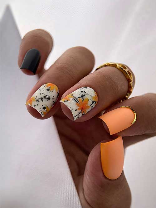 Matte orange, white, and green fall nails decorated with maple leaves and black speckles on the white nails