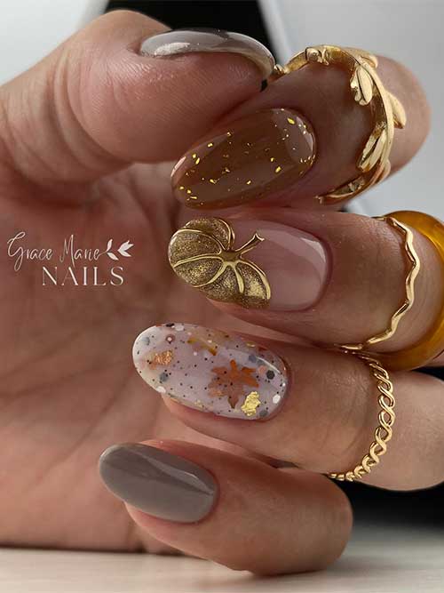 Short creative fall nail design features different brown nails adorned with glitter and a gold pumpkin and maple leaves