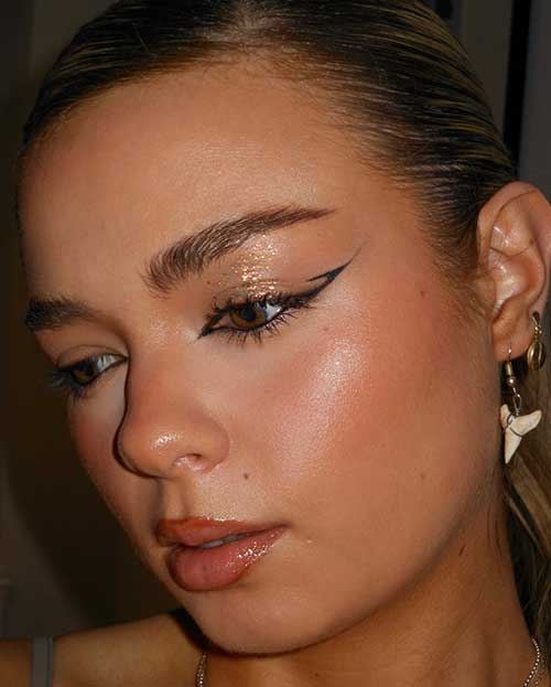 A beauty look features simple graphic eyeliner, shimmering glitter eyeshadow, and glossy nude lips for an elegant appearance.