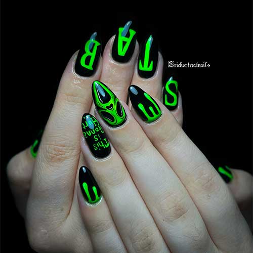 Black Halloween nails with a green scary face on an accent nail, “STAB” letters on four nails, and drip nail art on accents