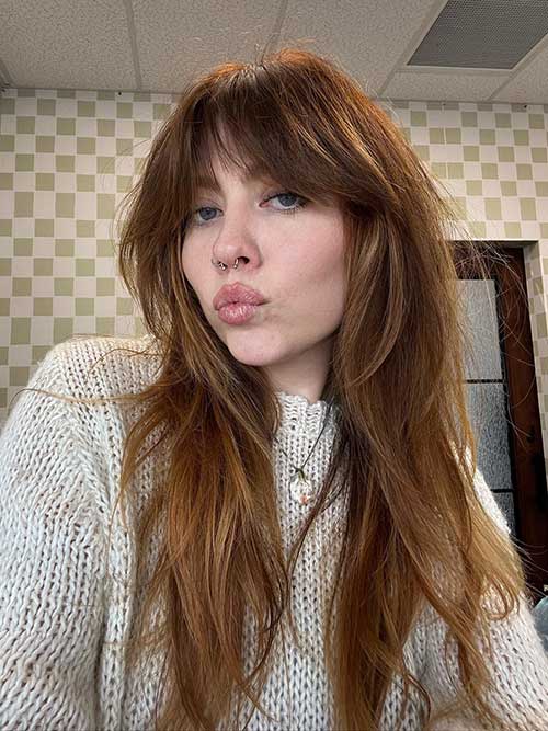 Long shaggy hairstyle featuring copper balayage and stylish curtain bangs, adding a vibrant touch to the look.