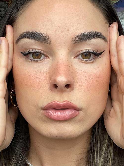 Faux freckles with black winged eyeliner and glossy nude lips create a chic back-to-school makeup look.