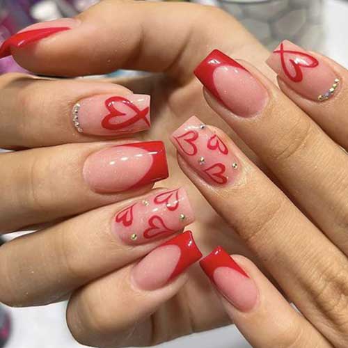 Medium red French tip press-on nails with heart design and rhinestones, perfect for Valentine's Day.