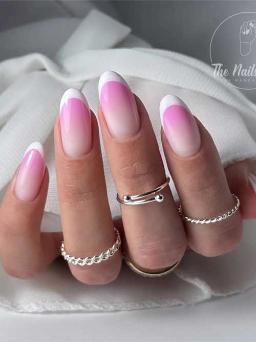 Almond-shaped nails feature a soft pink to vibrant pink ombre, topped with white French tips and paired with silver rings.