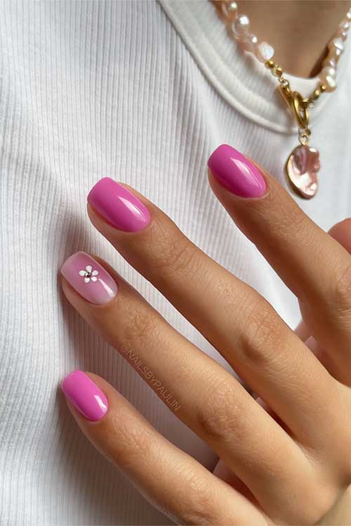 Glossy bright pink nails with an accent nail displaying a white floral motif on light pink, creating a fresh feminine look.