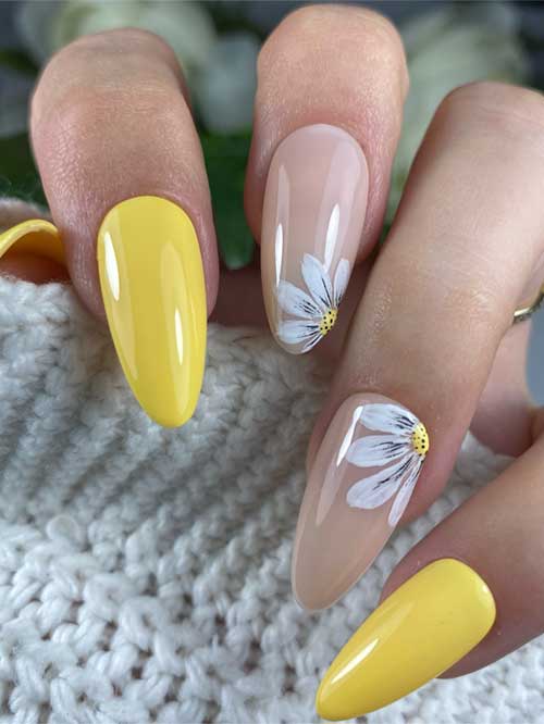 Glossy long almond spring nails with bright yellow polish, nude base, and delicate white daisies.