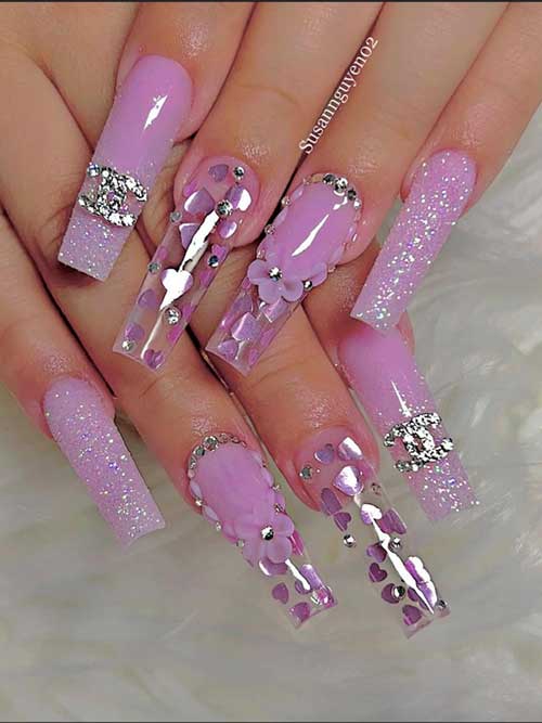 Long pastel pink nails with 3D floral designs, rhinestones, silver glitter, and heart accents, embodying spring's charm.