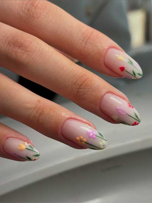 Spring nails with a soft pink base, featuring vibrant floral patterns and green stems for a fresh, elegant look.